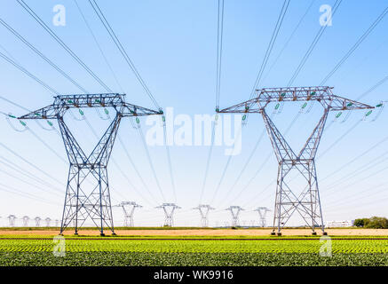 Vue de face de deux pylônes électriques dans la campagne française avec des dizaines d'autres pylônes au loin sous un ciel bleu clair. Banque D'Images