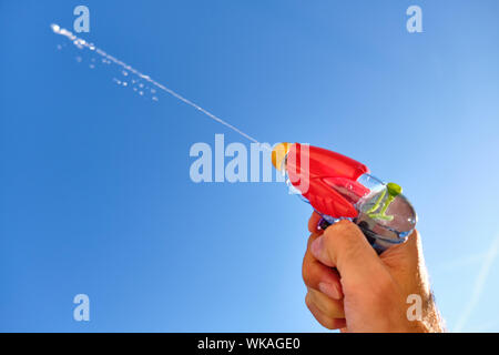 Pistolet à eau colorés à la pulvérisation d'un jet d'eau dans un homme de race blanche main devant le ciel bleu d'un jour d'été ensoleillé Banque D'Images