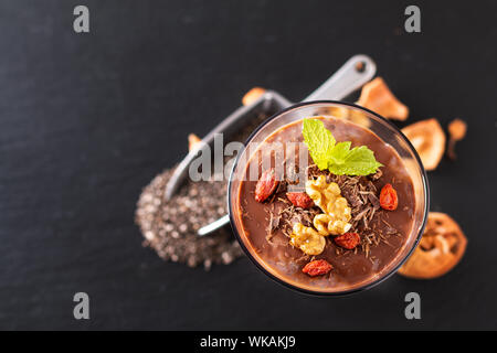 Concept d'aliments sains, les graines de Chia pudding au lait au chocolat et noix séchées goji en petit verre sur fond d'ardoise noire Banque D'Images