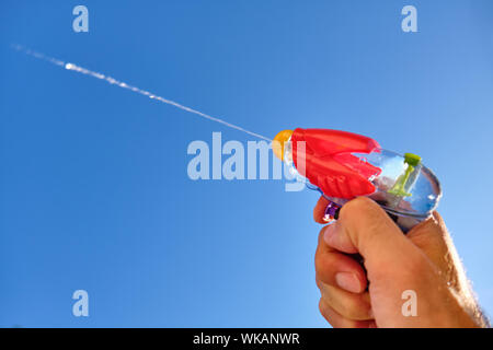 Pistolet à eau colorés à la pulvérisation d'un jet d'eau dans un homme de race blanche main devant le ciel bleu d'un jour d'été ensoleillé Banque D'Images