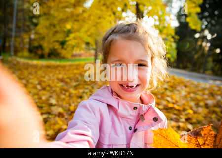 Jolie petite fille avec des dents manquantes en tenant. selfies Heureux l'enfant rire et sourire. Forêt d'automne ensoleillée, sun beam. Banque D'Images