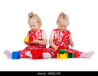 Les enfants et les jumeaux - deux lits jumeaux identiques in robes rouges Playing with toy blocks Banque D'Images