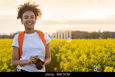 Beautiful happy mixed race African American girl adolescent femme jeune femme smiling outdoors avec dents parfaite de prendre des photographies avec un appareil photo dans un Banque D'Images