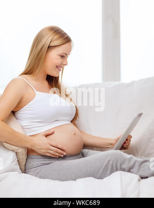 Grossesse, maternité, internet et technologie concept - smiling pregnant woman sitting on sofa with tablet PC ordinateur Banque D'Images