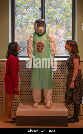 Wellcome Collection, London, UK. 4 septembre 2019. Une exposition sur ce que cela signifie d'être humain au 21e siècle. Divisé en quatre sections, la génétique, l'esprit et corps, l'infection, et de l'environnement ventilation, le nouveau système d'affichage présente environ 50 œuvres et objets qui reflètent nos espoirs et craintes à propos de nouvelles formes de connaissances médicales pour l'évolution de nos relations avec nous-mêmes, les autres et le monde. De droit : PPE Projet. Mary Beth Heffernan. Des tirages numériques affichées sur mannequin habillé dans des équipements de protection individuelle (EPI), 2015. Combinaison Hazmat personnalisé avec im Banque D'Images