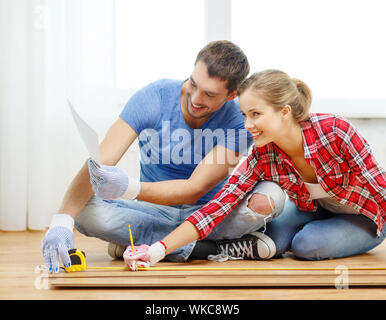 La réparation, de la construction et de l'accueil concept - smiling couple Mesure de bois de plancher Banque D'Images