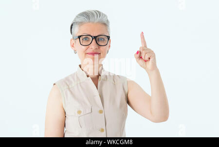 Idée ! Belle femme mature dans les verres points un doigt vers le haut en étant debout sur un fond clair. Banque D'Images