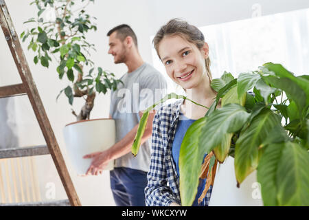 Jeune couple porte plantes vertes ensemble dans le nouvel appartement pour le déplacement ou déménagement dans Banque D'Images