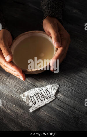 Clouseup d'un morceau de papier avec le mot otono automne, écrit en espagnol, sur une table en bois rustique gris et d'un jeune homme de race blanche l'échauffement avec un b Banque D'Images