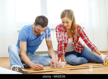 La réparation, de la construction et de l'accueil concept - smiling couple Mesure de bois de plancher Banque D'Images