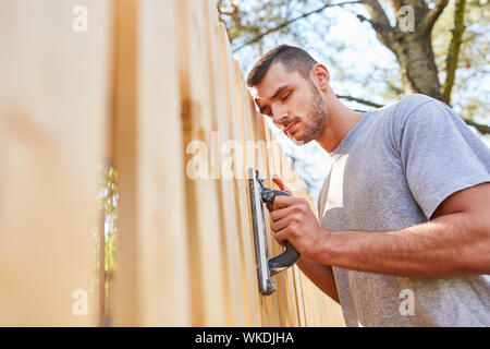 Jeune homme comme un artisan stagiaire ou comme un travailleur à la maison d'amélioration au niveau de la clôture grind dans le jardin Banque D'Images