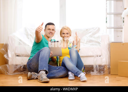 Déménagement, accueil, de la technologie et de couple concept - smiling couple assis sur le plancher avec tablette PC ordinateur showing Thumbs up in new home Banque D'Images