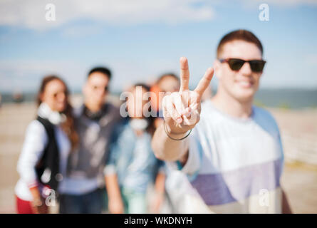 Vacances d'été et teenage concept - close up of male part montrant v-signe avec les doigts avec des amis sur l'arrière Banque D'Images