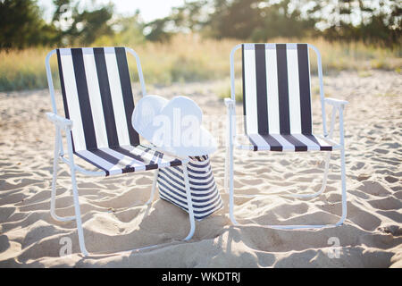 Les meubles et les vacances d'été - deux salons de plage avec sac de plage et chapeau blanc sur la plage Banque D'Images