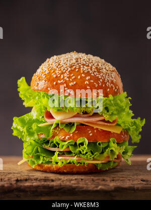 Big sandwich burger avec fromage, jambon et laitue sur un fond sombre. Banque D'Images