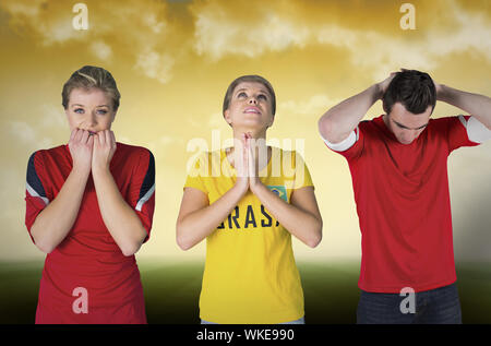 Image composite de plusieurs fans de football contre terrain de football sous ciel jaune Banque D'Images