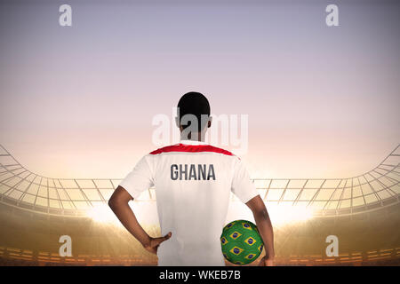 Ghana football player holding ball contre le grand stade de football under blue sky Banque D'Images