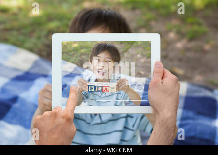 Hand holding tablet pc montrant happy boy holding alphabets bloc comme jouer au parc Banque D'Images