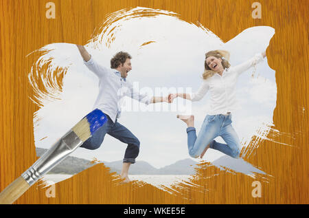 Image composite du couple jumping on the beach un pinceau trempé dans du bois bleu contre table en pin Banque D'Images