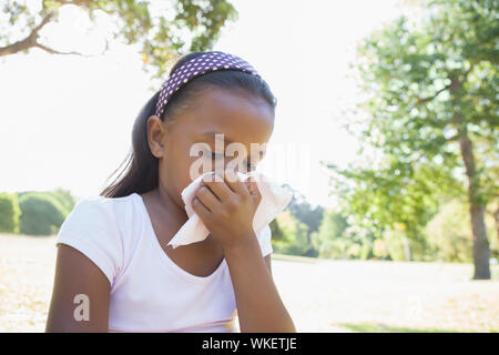 Petite fille assise sur l'herbe s'être mouché le nez sur une journée ensoleillée Banque D'Images