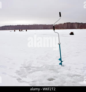 Percer la glace martelée dans la glace avec un trou sur l'arrière-plan d'un groupe de pêcheurs sur un lac gelé. Le concept de recherche active de poissons. Banque D'Images