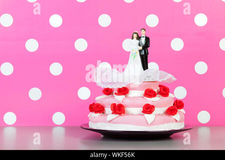 Couple sur le dessus de gâteau de mariage rose avec roses rouges isolated over white background Banque D'Images