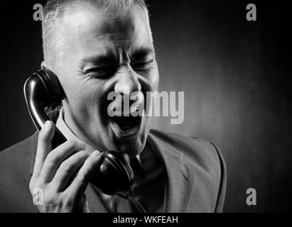 Bel homme tenant un récepteur téléphonique vintage sur fond sombre. Banque D'Images