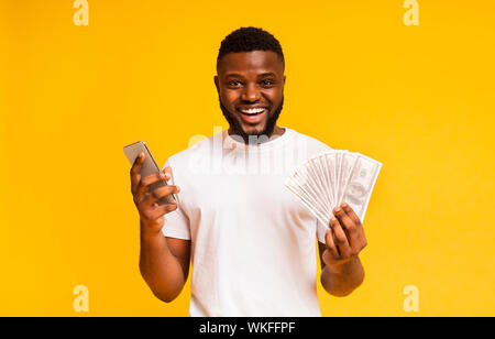 Happy african american guy holding cellulaire et un tas d'argent Banque D'Images