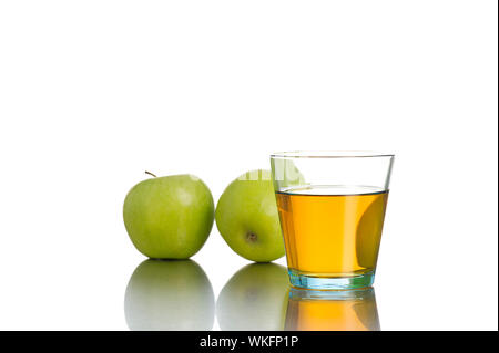 Seul petit verre avec jus en face de deux pommes vertes sur fond blanc Banque D'Images