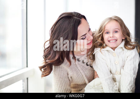 La famille d'amour heureux ensemble. La mère et l'enfant daughter hugging par la fenêtre portant des chandails confortables Banque D'Images