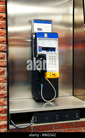 Public en acier inoxydable phone booth sur mur de brique rouge. Banque D'Images