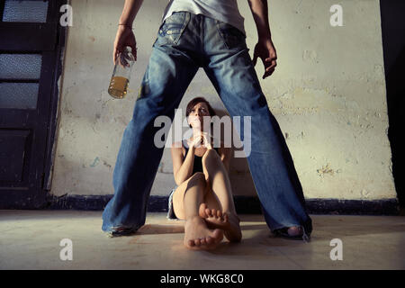 Les gens, l'abus et la violence domestique. Drunk man standing avec bouteille de whisky et menaçant sa jeune épouse à la maison Banque D'Images