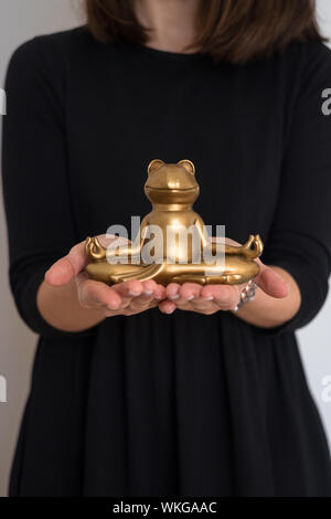 Woman's hands holding smiling gold yoga frog in lotus pose. Corps, l'âme et l'équilibre concept. Banque D'Images