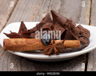 Morceaux de chocolat foncé avec le bâton de cannelle, la gousse de vanille et l'Anis Étoile sur plaque blanche isolé sur fond de bois Banque D'Images