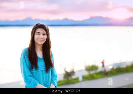 Belle jeune fille préadolescente bénéficiant à l'extérieur par le lac au coucher du soleil Banque D'Images