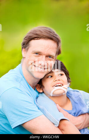 Beau père assis souriant avec son fils de 7 ans handicapés à l'extérieur Banque D'Images