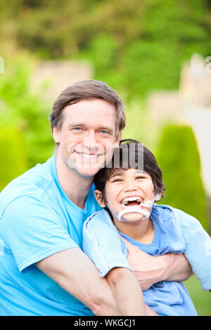 Beau père assis souriant avec son fils de 7 ans handicapés à l'extérieur Banque D'Images