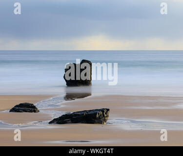 Une longue exposition photo de vagues se brisant sur les rochers sur la plage dans la baie de Sango à Durness. Rideaux de pluie dans la distance couvrant la Banque D'Images