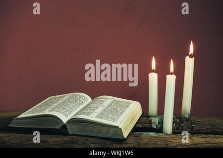 Belle bible ouverte et trois blancs brûlé des bougies sur une vieille table en bois de chêne et du mur. Banque D'Images
