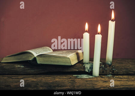 Belle bible ouverte et trois blancs brûlé des bougies sur une vieille table en bois de chêne et du mur. Banque D'Images