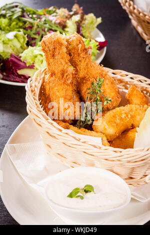 Des cuisses de poulet croustillantes ailes d'or et frits dans la chapelure et servi avec un bol de trempette dans un panier en osier pour un délicieux apéritif Banque D'Images