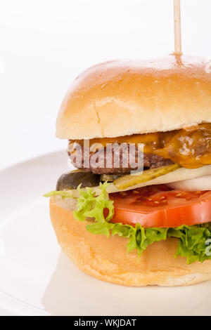 Savoureuse traditionnelle cheeseburger avec un sol recouvert de patty de boeuf fromage fondu et servi avec des rondelles d'oignon, tomate et laitue frisée sur un roun Banque D'Images