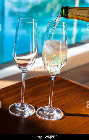 Vie de luxe Champagne vin mousseux réfrigérée versant verres de champagne /Cava/Prosecco sur vacances de vacances ensoleillée terrasse villa de luxe avec piscine à débordement de l'hôtel /en arrière-plan Banque D'Images