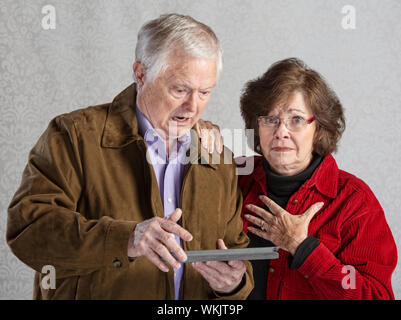 Homme en colère à l'aide de tablette avec femme embarrassée Banque D'Images