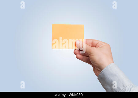 La main de l'homme en bleu clair shirt tenir une note adhésive blanc orange sur blanc dégradé à fond bleu clair Banque D'Images