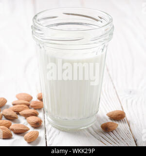 Du lait ou du yogourt en pot Mason sur table en bois blanc, avec des amandes de côté Banque D'Images