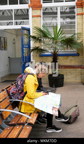 Voyageur de l'adolescence avec l'iphone s'asseoir sur un banc dans une gare en regardant une carte avec un ami portant un sac à dos et mac jaune UK KATHY DEWITT Banque D'Images