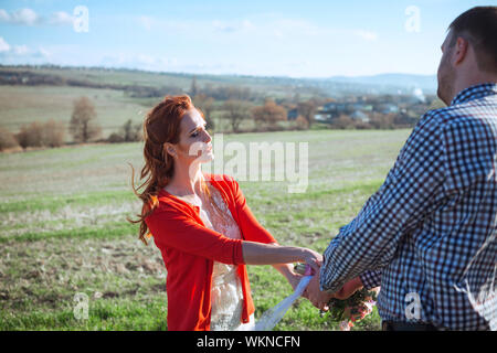 Heureux mariés le jour de leur mariage. mariage en couple ville décontractée est debout sur un champ vert sur l'arrière-plan de la forêt au coucher du soleil, la mariée Banque D'Images