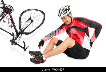 Biker asiatique est tombé de vélo, blessé au dos douloureux avec l'expression du visage, assis sur le plancher, isolé sur fond blanc. Banque D'Images