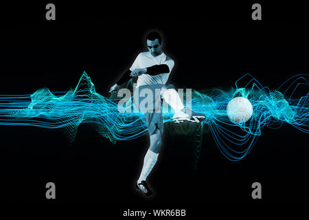 Joueur de football en blanc kicking against abstract blue fond noir brillant Banque D'Images